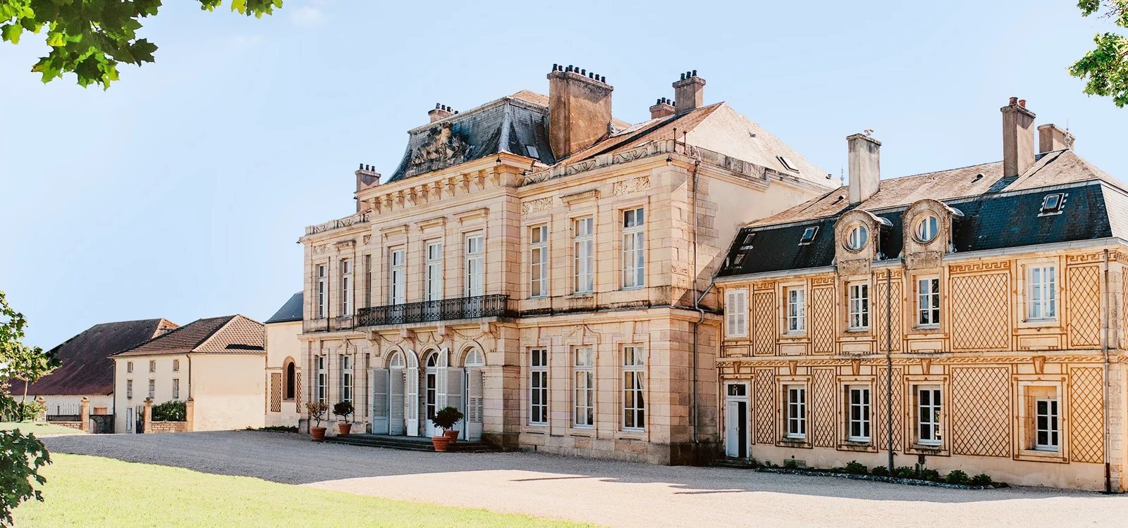 Façade du château d’Arcelot, cour et arbres au premier plan.