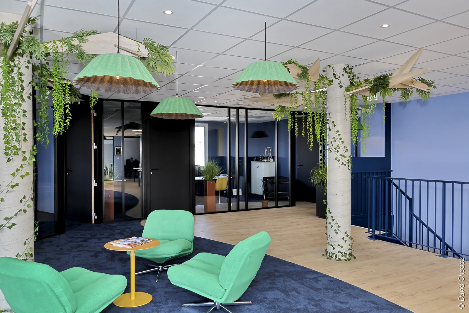 Espace détente et travail Ektor : fauteuils verts, tables, cloisons vitrées et luminaires végétalisés.