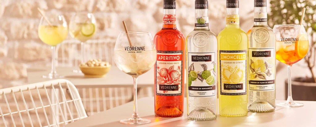 Bouteilles de liqueurs Vedrenne et cocktails Spritz sur une table de terrasse.