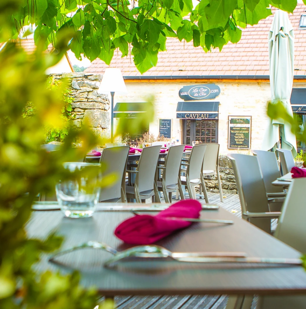 La terrasse du restaurant Le Clos Napoléon, avec ses tables dressées et sa façade en pierre sous la verdure.